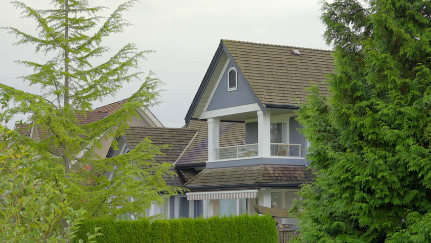 Establishing shot. Top of grey stucco luxury house with shingle roof, red and yellow trees and nice windows in Fall in Vancouver, Canada. Day time on October 2024. Still camera view. ProRes 422 HQ.