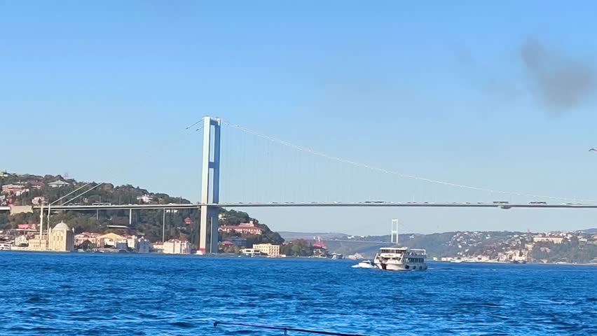 Istanbul's Bosphorus Bridge: Connecting Continents, Inspiring Journeys.A scenic view of the Bosphorus Bridge in Istanbul, Turkey, with a passenger ferry navigating the vibrant blue waters. 4k fullhd