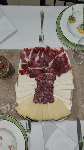 Plate with ham, sausage and two types of cheese on a table prepared for several diners