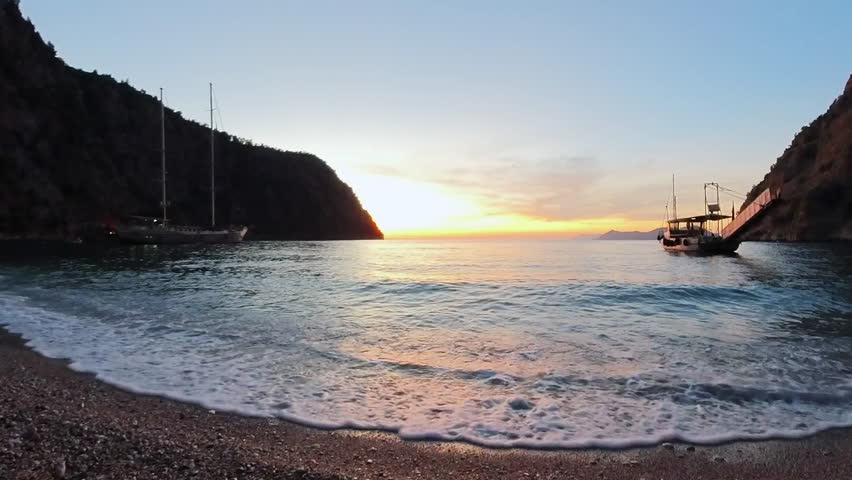 A tranquil scene capturing the peaceful sunset over Butterfly Valley Beach in Turkey, with soft golden light illuminating the calm waters and rugged cliffs in the background.