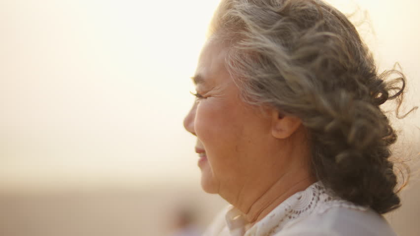 4K Portrait of Happy Asian senior woman relaxing and looking beautiful nature of tropical island beach at sunset. Elderly woman enjoy outdoor lifestyle travel at the sea on summer holiday vacation.
