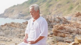 Asian senior man practicing meditation with ocean nature on rocky coastal hill at summer sunset. Retirement elderly people do outdoor relaxing yoga exercise. Mental health care and motivation concept. - Powered by Shutterstock - Get 15% off with code: PIKWIZARD15