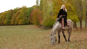 Girl is sitting on horse while it is grazing.