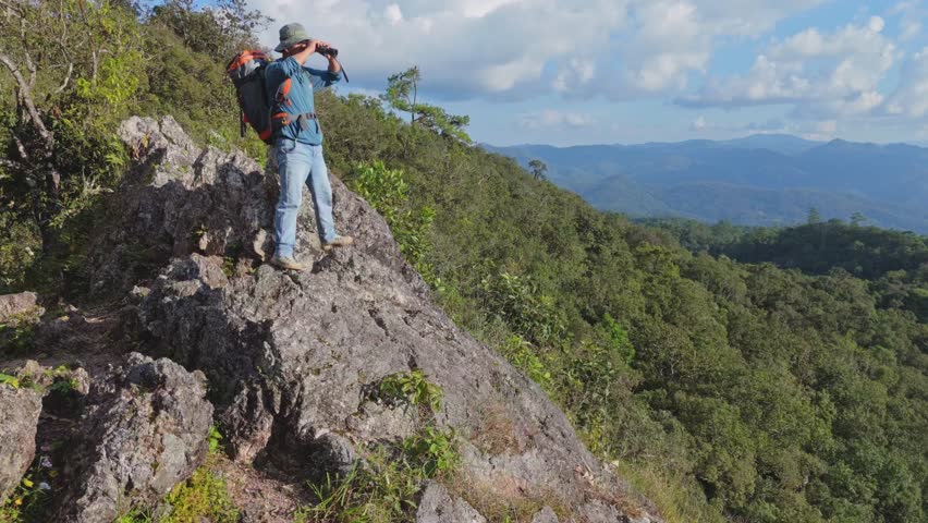Hikers with backpacks holding binoculars looking on top of the rock mountain