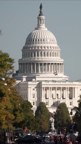 Vertical Video view of the US Capitol building in Washington DC with fall foliage in the foreground and traffic lights and street signs in the foreground.
