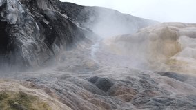 Witness the breathtaking beauty of Mammoth Hot Springs' geothermal terraces, showcasing vibrant mineral deposits and steam rising from the earth under a cloudy sky. - Powered by Shutterstock - Get 15% off with code: PIKWIZARD15