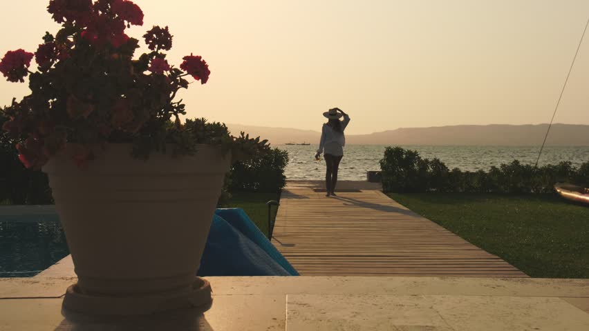 A woman is walking on a wooden boardwalk near a body of water, luxury tropical resort