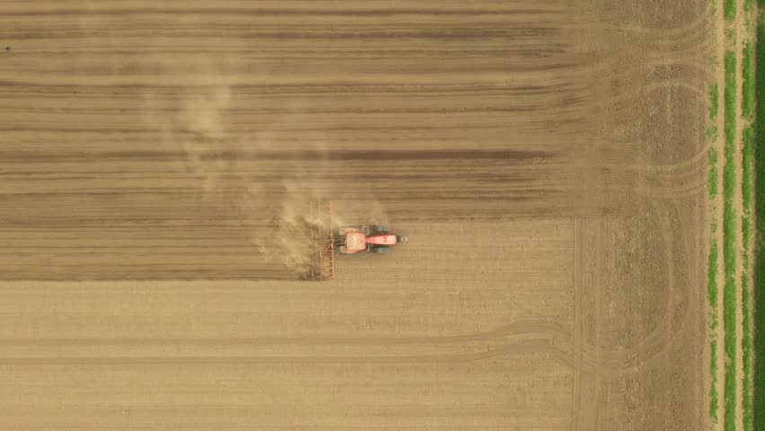 Above top view of tractor as pulling machine, harrowing arable field, shreds the earth to preparing soil for planting new crop next season.