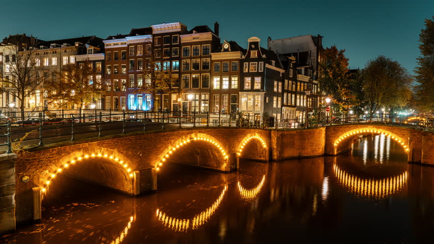 Timelapse of Amsterdam’s historic canal bridges illuminated at night. The Keizersgracht and Reguliersgracht intersection glows beautifully, reflecting typical Dutch architecture in the water