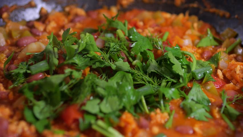 Sprinkling herbs garlic dill and parsley over chili con carne. Close up.