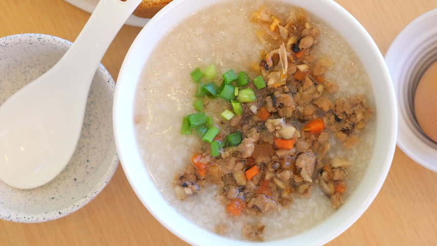 Traditional Asian rice porridge with minced meat, chopped vegetables, and green onions on wooden table. Comfort Food and Asian Cuisine.