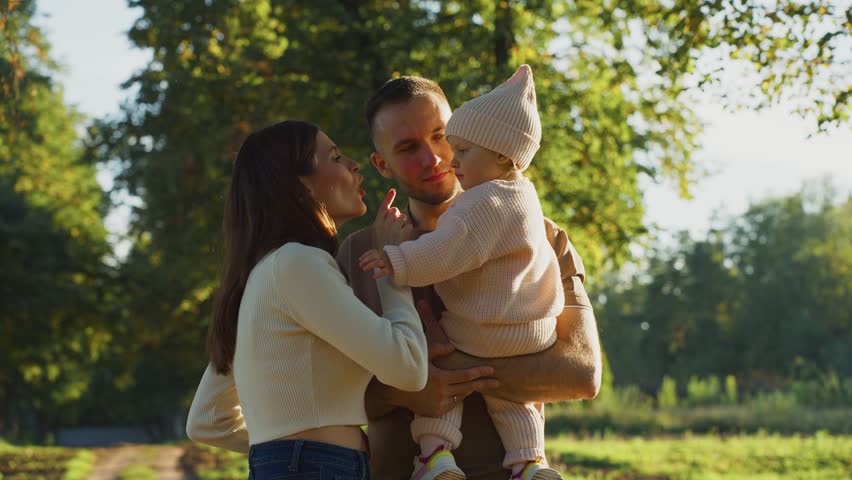 A young family shares a joyful moment in a park, surrounded by autumn foliage. The couple lovingly interacts with their baby, creating happy memories in nature.