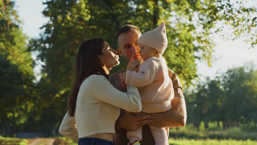 A young family shares a joyful moment in a park, surrounded by autumn foliage. The couple lovingly interacts with their baby, creating happy memories in nature.