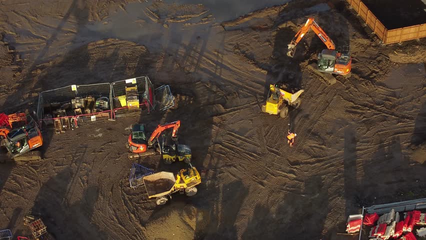 Construction machinery building new property development aerial view tilt down to muddy housing site