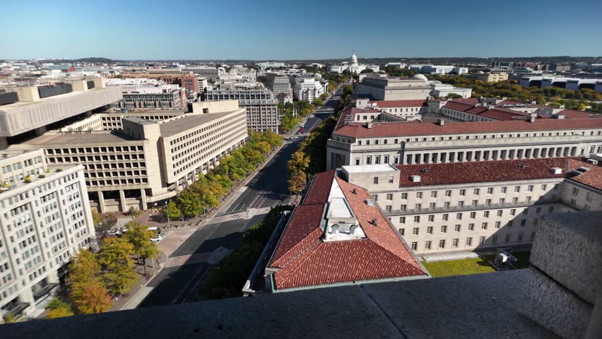 Aerial view of Washington DC featuring a cityscape with various buildings, including the iconic Capitol Building, a street lined with trees, and a large government building with a tiled roof.
