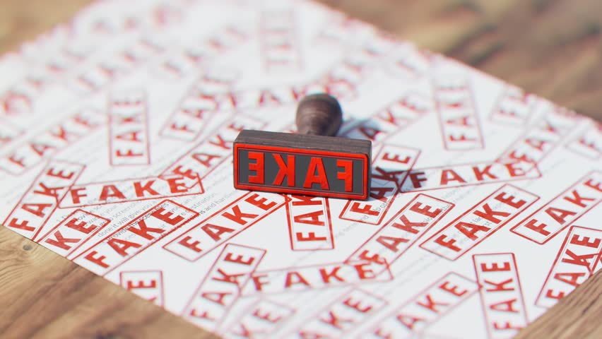 Wooden stamp with multiple red texts FAKE stamped on the document. False papers checked. Fraud, fake news, fake covid vaccination concept. Paperwork deception. Verification of the authenticity.
