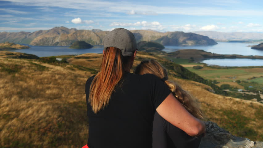 Mother and daughter on hike enjoy New Zealand landscape view, close-up pan from behind