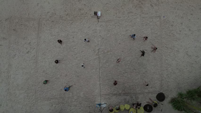 Top-down aerial view of children playing football on an improvised sandy beach playground, surrounded by palm trees in a serene tropical setting. Location Philippines.
