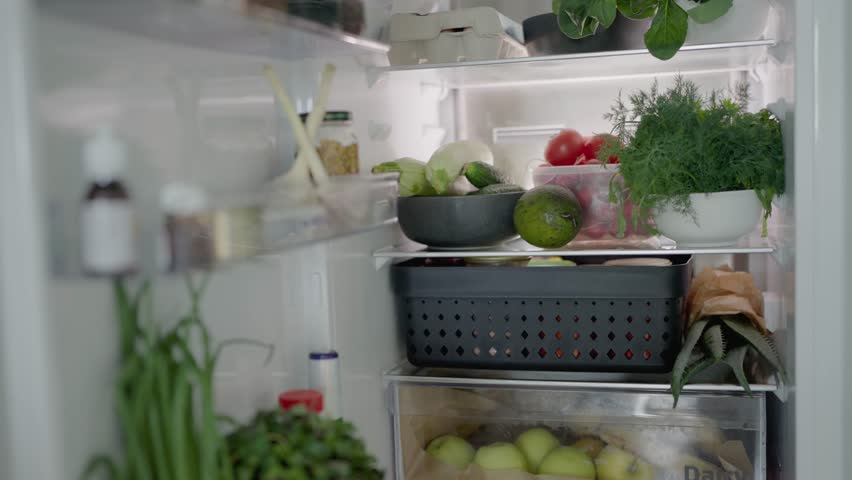 A well-organized refrigerator filled with fresh vegetables and herbs, showcasing healthy ingredients including cucumbers, tomatoes, avocados, and leafy greens.