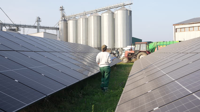 Female farmer with digital tablet on a modern farm using solar panels. Agricultural silos in the background