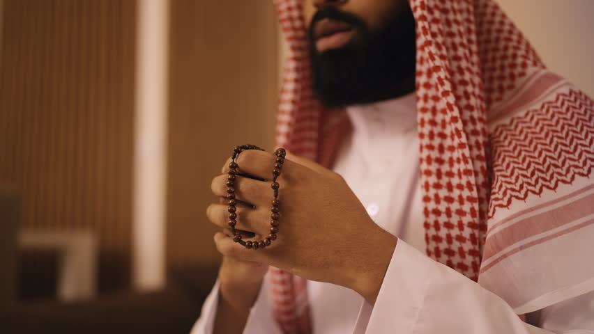 Arab man in traditional ghutrah headscarf praying with beads in hands, religion