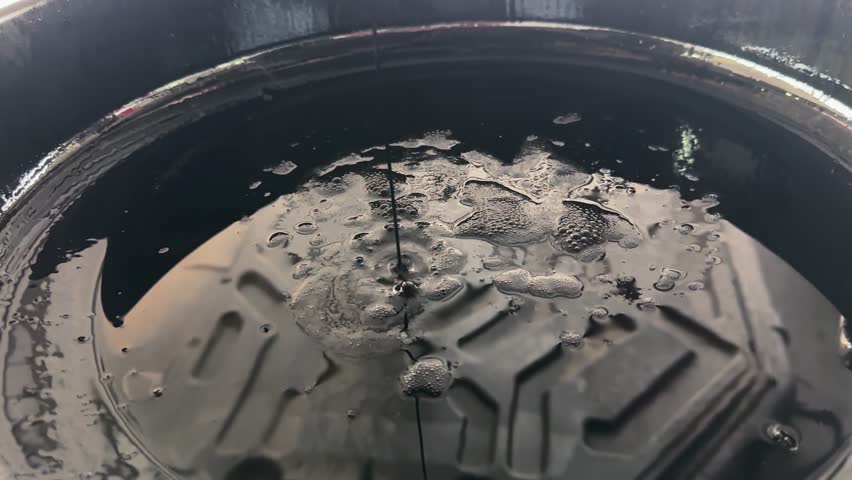 Close-up of motor oil pouring from a car engine into garbage disposal container. Motor oil being poured into a car engine, highlighting the texture and reflections of the oil with precision.