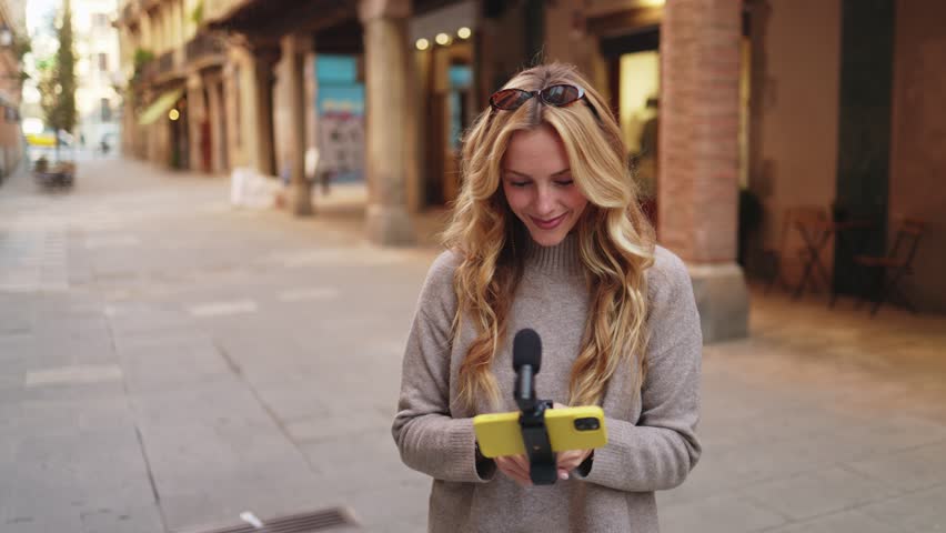 Young woman vlogging on city street using a smartphone gimbal to create engaging travel content.    Influencer creating content with smartphone gimbal