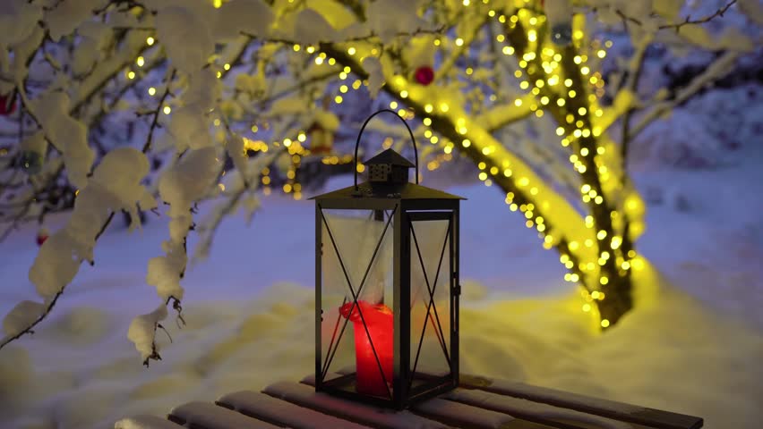The cozy snow-covered courtyard of the house decorated with Christmas lights and candles.