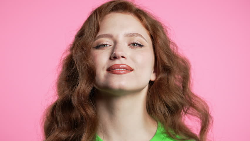 Gorgeous woman in green outfit showing yes signal, nods head, approve. Positive smiling european girl, body language. Correct perfect choice, great deal. Pink studio background
