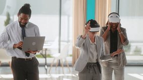 Black businessman using laptop presenting project through virtual reality glasses for his two female multi-ethnic colleagues during a meeting.  Virtual reality business presentation - Powered by Shutterstock - Get 15% off with code: PIKWIZARD15