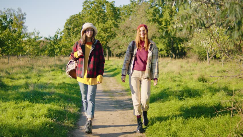 Two close friends are enjoying a sunny day outdoors, surrounded by nature. They bond while walking a scenic path, experiencing joy and laughter during this memorable spring weekend