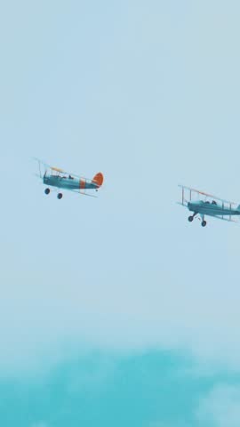 Two retro biplane planes fly high in the sky together, vertical video