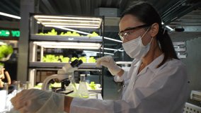 A scientist wearing a mask and gloves works in a lab, examining a green liquid in a beaker and using a microscope. The lab setup is well-lit, reflecting a focus on research, science, and experimentati - Powered by Shutterstock - Get 15% off with code: PIKWIZARD15