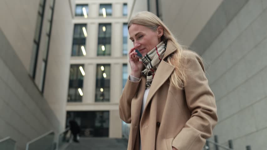 Young woman in a stylish coat talking on the phone in an urban setting during a bright morning