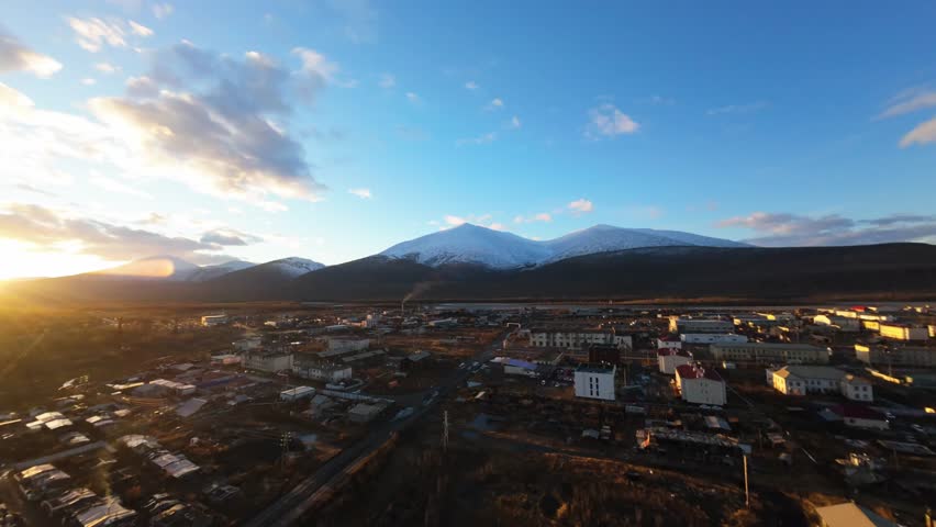 As the sun sets, it casts a warm glow over the snowy mountains and a quaint town nestled in the valley. A perfect blend of nature and serenity unfolds during this enchanting dusk.