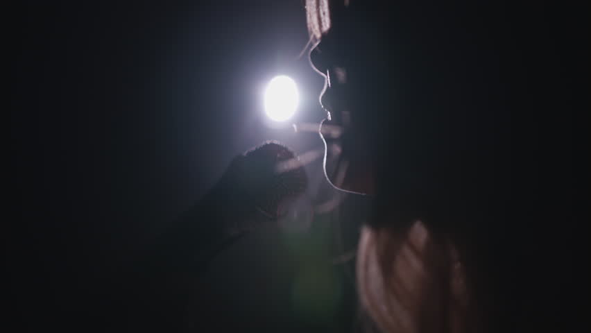 Close-up of the face of the singer with microphone on a black smoky background. The singer sings a song on stage in the dark, smoke, purple light, concert.
