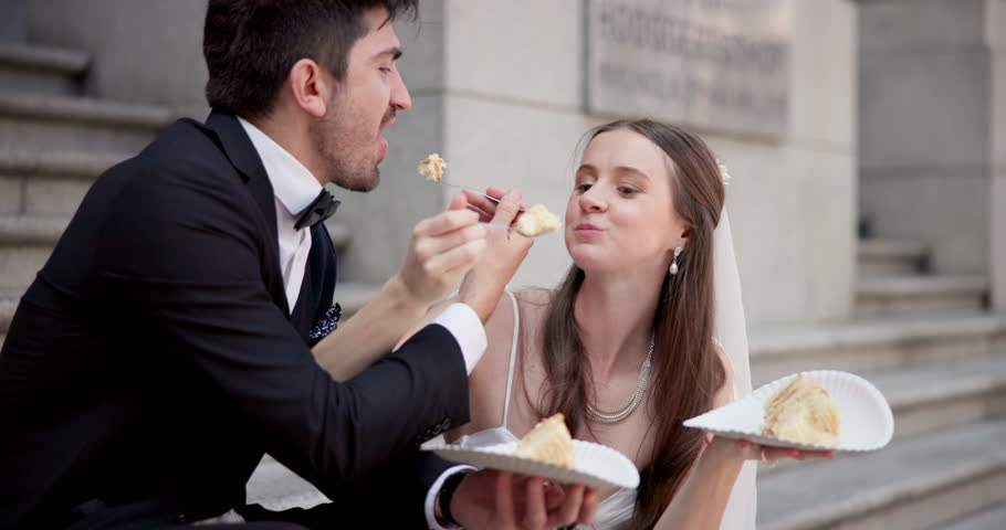 Outdoor, wedding cake and couple with love, eating and bonding together with happiness. Outside, stairs and bride with groom, relationship and sweet treat with humor, care and cheerful with marriage