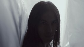 Handsome man with long hair posing at camera with serious expression between flowing plastic curtains in studio with soft backlighting. Video portrait - Powered by Shutterstock - Get 15% off with code: PIKWIZARD15