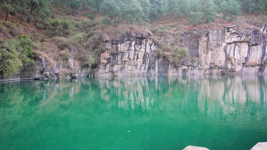 A serene emerald lake surrounded by towering, vertically striped cliffs. The unique geological formation and tranquil waters create a breathtaking natural masterpiece. Antsirabe, Madagascar.
