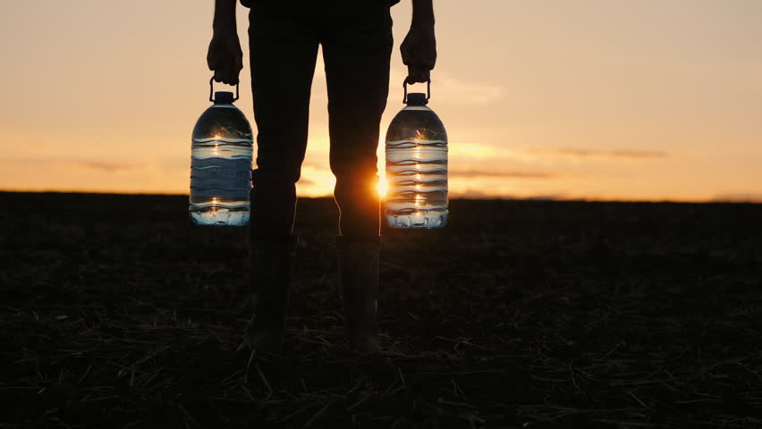 In the glow of the sunset, a man is seen holding two bottles of drinking water in a field.