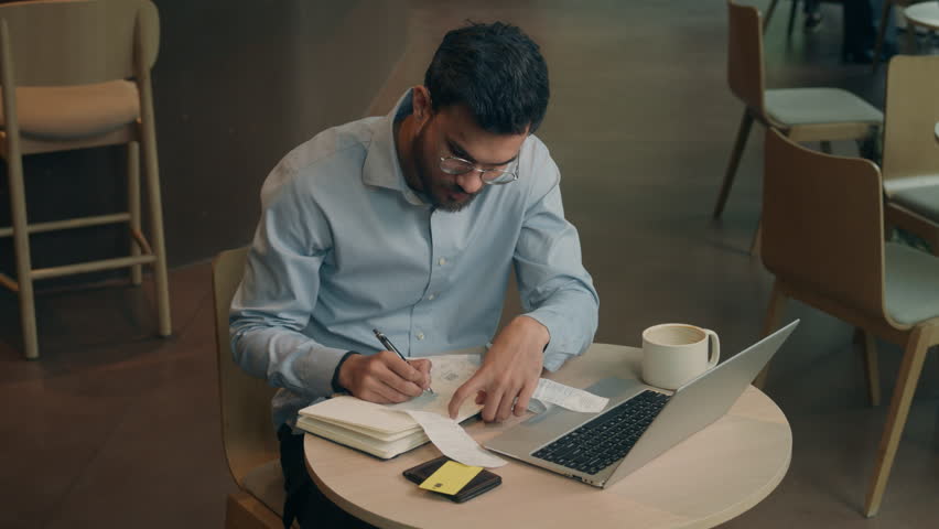 Arabian Indian businessman in cafe online work laptop pay bills read count high taxes payment debt bankruptcy male stressed business man guy client shock upset frustrated count finance write paperwork