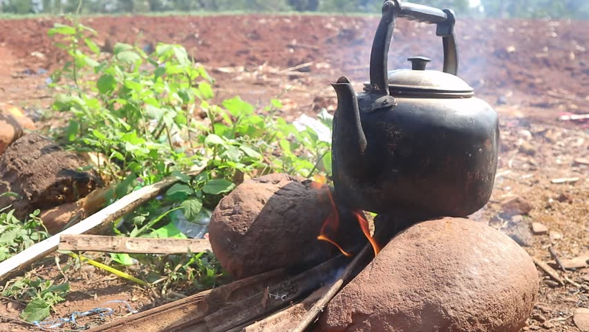 Boiling water in a blackened kettle over a stone stove in a field or open area.