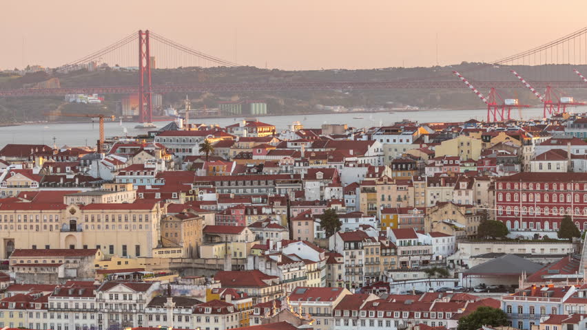 Tagus River and Bridge April 25 or Ponte 25 de Abril aerial timelapse above Orange Roofs of houses in Lisbon, Portugal. Panoramic view from viewpoint Miradouro da Senhora do Monte during sunset