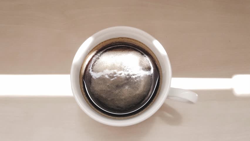 A cup of coffee on a wooden table and sunlight reflection