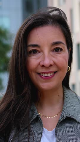 Vertical. Mature Caucasian business woman looking smiling at camera in formal wear standing happy outdoor. Empowered adult commercial professional female posing in confident attitude in city workplace