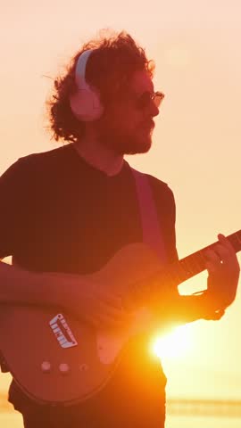 Hipster street musician in black playing electric guitar in street outdoors on sunset with lens flare