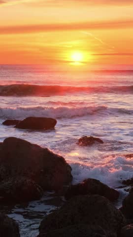 Atlantic ocean sunset with waves and rocks and surfers silhouettes in water at Costa da Caparica, Portugal