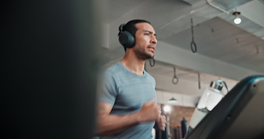 Man, training and running on treadmill for exercise, fitness or cardio workout with headphones at gym. Active, runner and sports person with endurance, health podcast and athlete challenge with music