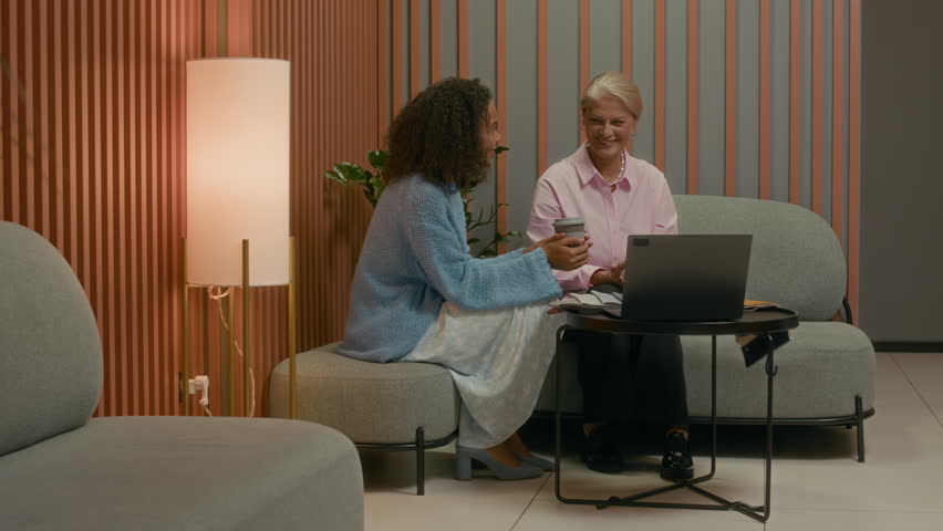 Diverse team of three creative professionals cooperating on project in sleek design office space, sitting by laptop, all involved in discussion