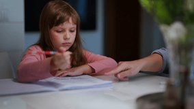 Young girl in a pink shirt attentively working on homework with a parent's guidance at the table, focused on her task with a pencil in hand. Concept of learning, education, and tutoring - Powered by Shutterstock - Get 15% off with code: PIKWIZARD15